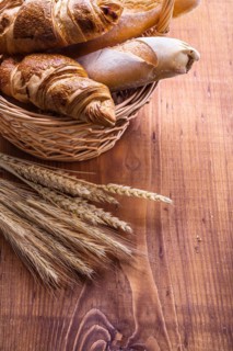 Close-up of baguettes and croissants in a wicker basket with ears of wheat