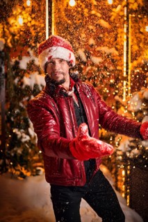 Man dressed as Santa Claus throws up snow on a street decorated with garlands. New Year and Christmas concept. Mixed media