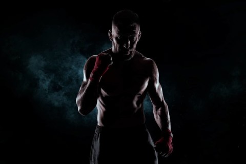Kickboxer in red bandages poses against a background of smoke. The concept of mixed martial arts. MMA