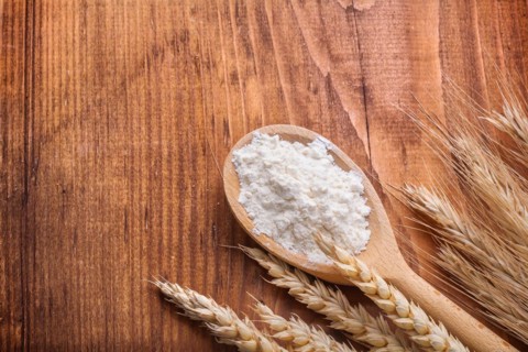 Flour in wooden spoon with ears of wheat on wooden table with copy space