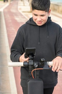 Front view 14-17 years old smiling happily riding electric scooter on the bike lane and using smart phone music apps