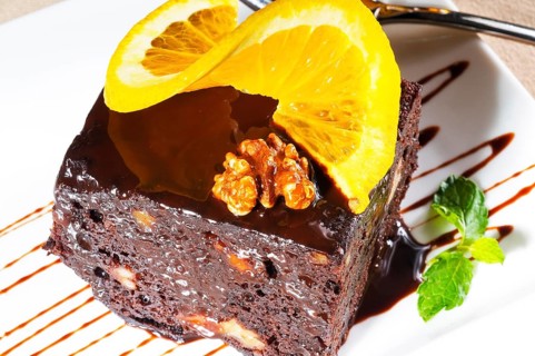 Fresh baked delicious chocolate and walnuts cake with slice of orance on top and mint leaf