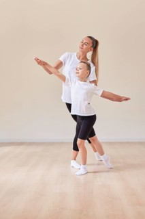 Beautiful woman teacher and a little girl perform dance movements in a bright studio. The concept of education