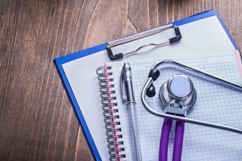 Medical stethoscope with purple tubes on clipboard with biros and vintage wooden board horizontal version medical comcept