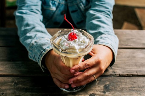 Female hand holding cherry milkshake on wooden table. Person holding cherry smoothie over wooden table