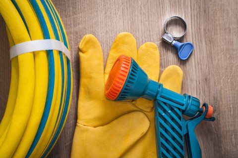 Hand spraying rubber hose with spray nozzle leather safety gloves and saddle clamp on wood board gardening concept