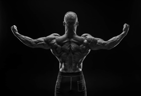Silhouette of a strong bodybuilder. View from the back. Confident young fitness athlete with a powerful body and perfect abs. Black and white photography. Dramatic light