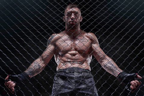 Dramatic image of a mixed martial arts fighter standing in an octagon cage. The concept of sports