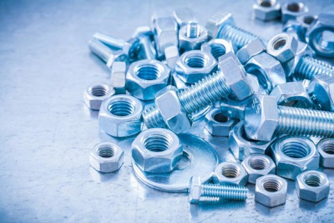 Big stack of metal threaded screwbolts nuts and bolt washers on metallic background construction concept