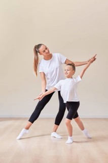 Beautiful woman teacher and a little girl perform dance movements in a bright studio. The concept of education