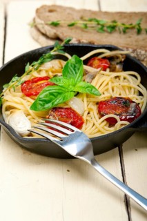 Italian spaghetti pasta with baked tomatoes basil and thyme sauce on a cast iron skillet
