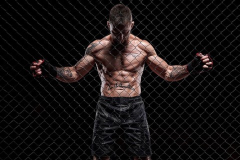 Dramatic image of a mixed martial arts fighter standing in an octagon cage. The concept of sports