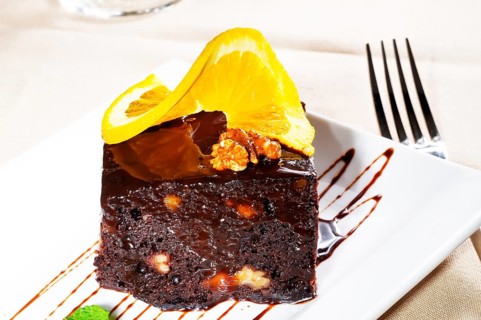 Fresh baked delicious chocolate and walnuts cake with slice of orance on top and mint leaf
