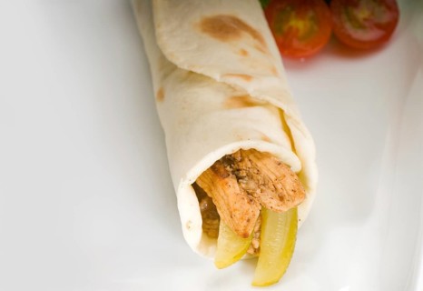 Pita bread chicken roll with pickles cucumbers on a plate with pachino tomatoes and lettuce