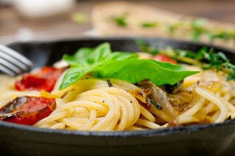Italian spaghetti pasta with baked tomatoes basil and thyme sauce on a cast iron skillet