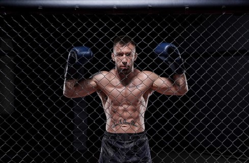 Dramatic image of a mixed martial arts fighter standing in an octagon cage. The concept of sports