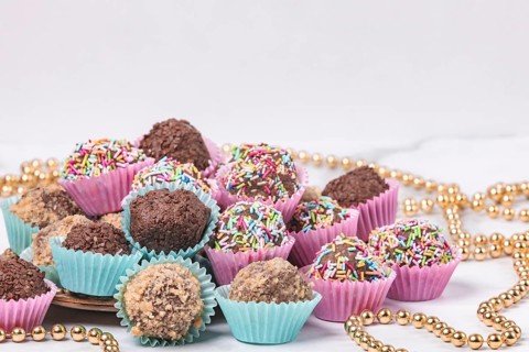 Dark rum balls with various sprinkles in pink and turquoise paper moulds