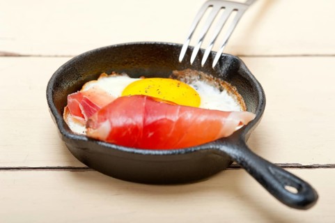Fried egg sunny side up with Italian tyrolean speck smoked ham on a skillet