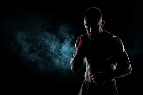 Kickboxer in red bandages poses against a background of smoke. The concept of mixed martial arts. MMA