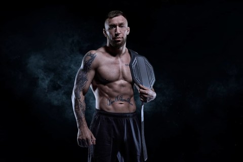 Kickboxer with a belt on his shoulder poses against a background of smoke. Sports competitions. Fight night. The concept of mixed martial arts. MMA
