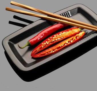 Fresh red chili peppers on a plate with chopstikcs over grey reflective surface