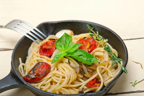 Italian spaghetti pasta with baked tomatoes basil and thyme sauce on a cast iron skillet