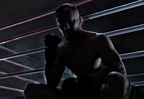 Kickboxer is sitting near the ring and motivatingly shows his fist in the overlay. Sports competitions. Fight night. The concept of mixed martial arts. MMA