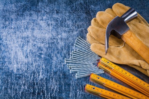 Copy space image of leather working gloves nails wooden measuring meter and claw hammer on scratched metallic background construction concept