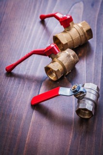Three plumbing fittings with red handles on an old wooden board