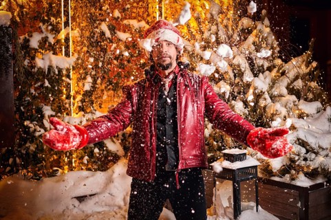 Man dressed as Santa Claus throws up snow on a street decorated with garlands. New Year and Christmas concept. Mixed media