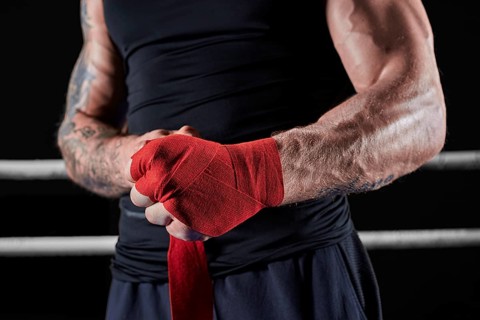 Red bandages on the hands of a kickboxer against the background of the ropes of the ring. The concept of mixed martial arts. MMA