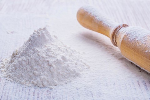 A small pile of natural white flour and a wooden rolling pin