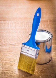 Brush with blue handle stands next to a tin on a wooden board