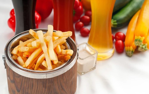 Fresh french fries on a wood bucket with selection of beers and fresh vegetables on background