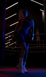 Powerful girl poses near the bag on the background of the ring. Color flashes. The concept of wrestling and boxing. Mixed media