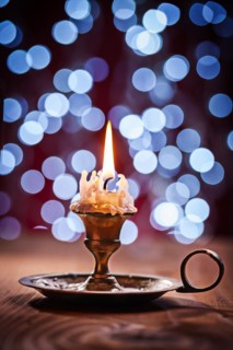 Burning candle in vintage brass candlestick standing on old wooden board