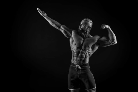Silhouette of a strong bodybuilder. Confident young fitness athlete with a powerful body and perfect abs. Black and white photography. Dramatic light. Mixed media