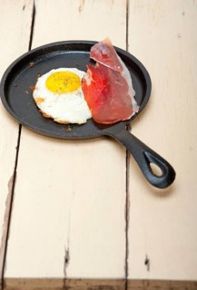 Fried egg sunny side up with Italian tyrolean speck smoked ham on a skillet