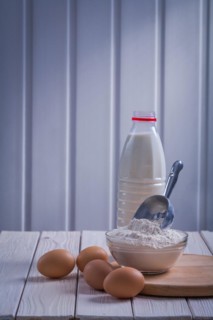 Eggs Flour scoop into bowl Bottle of milk on white lacquered old wooden board Eating and drinking concept