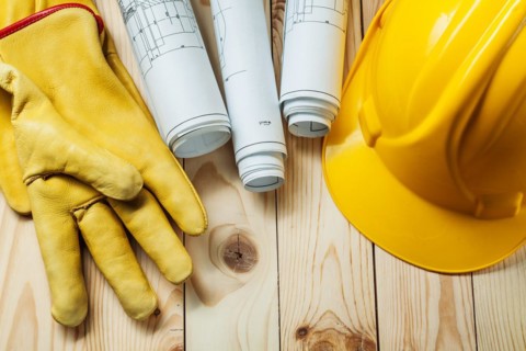 Yellow gloves blueprints and construction helmet on wood