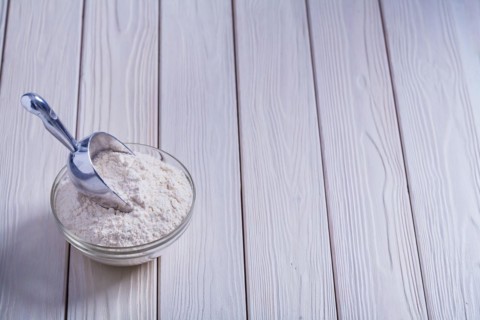 Bowl with flour and shovel on white lacquered old wooden board Food and drink concept