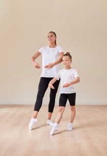 Beautiful woman teacher and a little girl perform dance movements in a bright studio. The concept of education