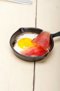 Fried egg sunny side up with Italian tyrolean speck smoked ham on a skillet