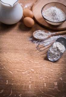 Flour in scoop Spoon and bowl Eggs Pitcher of milk on wooden board