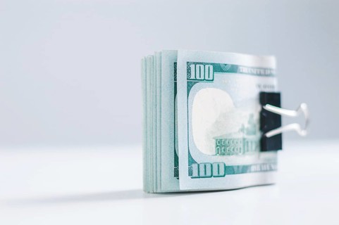 Pack of hundred-dollar bills lies on a white table fastened with a paperclip. The concept of savings during the crisis.