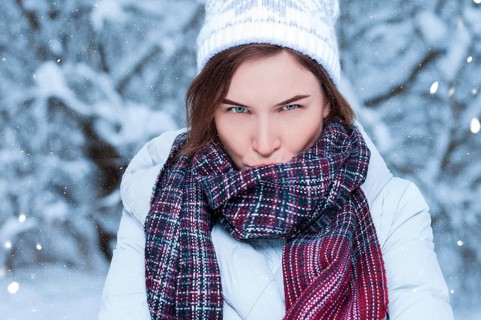 Beautiful girl with a displeased expression on the background of snowy trees. Snowball game. Christmas holidays concept.