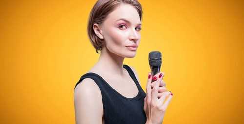 Portrait of an elegant stylish woman with a microphone. Yellow background. Karaoke concept.