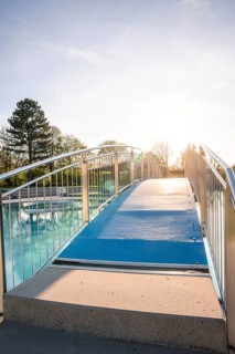 Blue pedestrian bridge over a swimming pool with a clear sky in the background