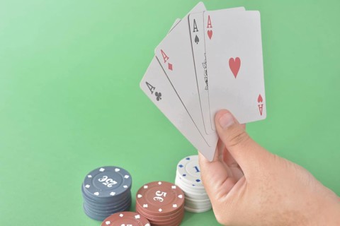 Four aces in a hand with various denomination poker chips on a green felt background