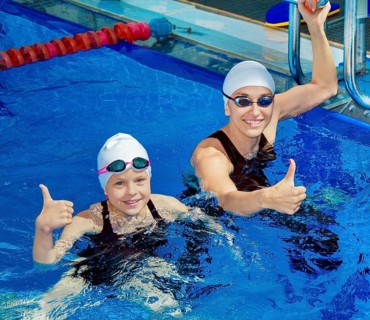 Charming coach with his student swimming in the pool and smiling
